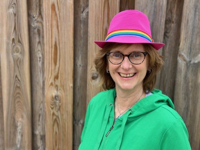 Celest, lachend met een vrolijke hoed met regenboog en roze op
